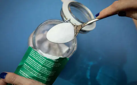 Ein Löffel Natron wird über ein Glas gehalten. Ein natürliches Hausmittel zur Geruchsneutralisierung und Reinigung.