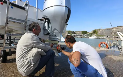 Deux hommes vérifient le montage moteur hors bord sur tableau arrière d'un bateau, près d'un port.