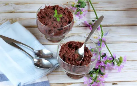 Dos copas de delicioso mousse de chocolate de la abuela, decoradas con menta y flores moradas, listas para disfrutar.