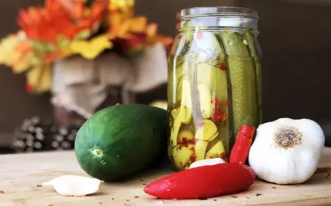 Słoik z ogórkami z chili w plastrach, obok świeży ogórek, czosnek i papryczka chili.