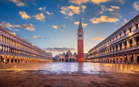Le **place Saint-Marc à Venise** s'illumine sous un ciel de fin de journée. La basilique et le campanile se dressent majestueusement.