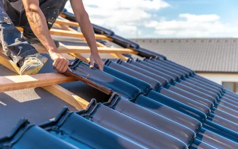 Un couvreur installe des tuiles sombres sur une toiture en bois. Un travail minutieux pour l'entretien de toiture.