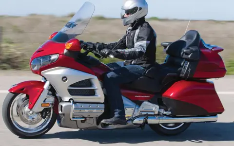 Mężczyzna w kasku jedzie lśniącym, czerwonym motocyklem turystycznym Honda Gold Wing.