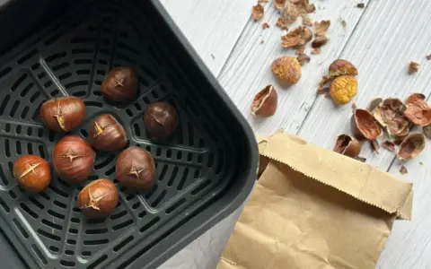 Châtaignes grillées dans le panier de l'air fryer, prêtes à être dégustées. Les écorces vides jonchent la table.