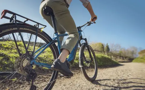 Fahrer auf einem blauen E-Bike mit Shimano Linkglide Schaltung genießt eine Fahrt auf einem Feldweg.