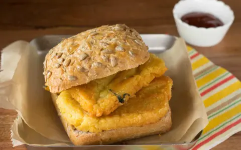 Panino con pane e panelle fritte, un classico street food siciliano, servito su un vassoio con carta da forno e una ciotolina di salsa.