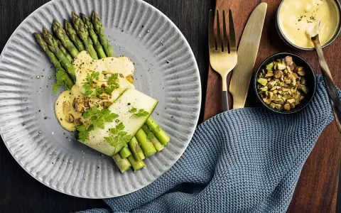 Une belle recette d'asperges vertes, nappées d'une sauce crémeuse et garnies de pistaches concassées. Un délice visuel et gustatif.