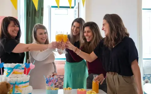 Kobiety świętują baby shower, wznosząc toasty. Widać tort z pieluch i dekoracje. Idealny strój na baby shower to coś wygodnego i eleganckiego.
