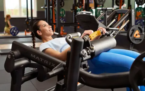 Femme souriante effectuant un hip thrust sur une machine de musculation, concentrée sur son entraînement.