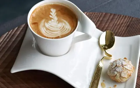 Ein Latte Macchiato mit schönem Milchschaum-Muster und ein Mandelgebäck, perfekt zum wiener Zubereiten.