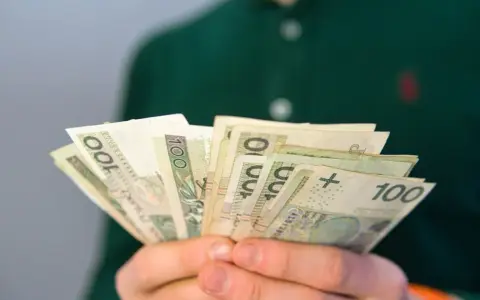Dłonie trzymają wachlarz banknotów 100 zł. Może to być pomoc finansowa, np. renta po zmarłym ojcu, która zapewnia wsparcie.