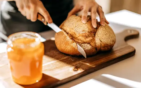 Händerna skär ett nybakat bröd på en skärbräda bredvid en burk sylt. En stund att visa tacksamhet för hemmets enkla glädjeämnen.