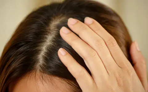 Main d'une femme effleurant son cuir chevelu, peut-être pour vérifier un kyste ou une irritation.