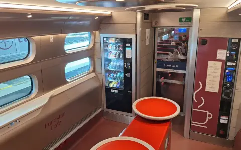 Interior of a Eurostar train from Amsterdam, featuring a cafe area with vending machines, seating, and windows looking out onto the tracks.