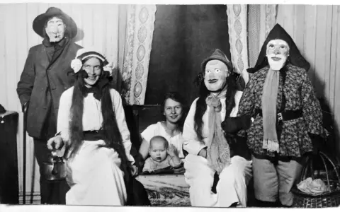 En familj klädd i masker och dräkter, kanske en del av julens historia, poserar för ett fotografi. En bebis sitter i förgrunden.