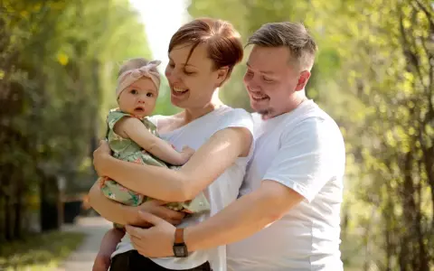 Szczęśliwa rodzina z córeczką w letnim parku. Mama tuli dziecko, tata obejmuje ich. Idealne babciowe warunki na spacer.