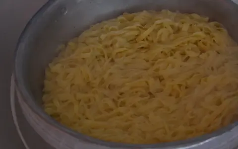 Gotowanie kluski vs makaron. Szerokie, żółte wstążki w garnku, gotowe do podania.