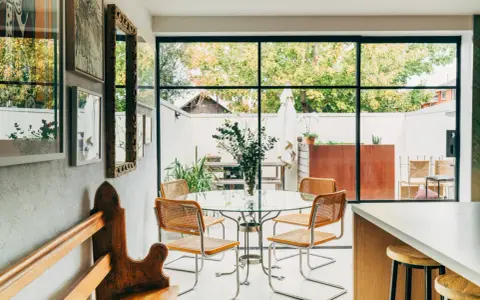 Sedie in paglia e metallo, ispirate a Marcel Breuer, attorno a un tavolo di vetro in una luminosa sala da pranzo con vista sul giardino.