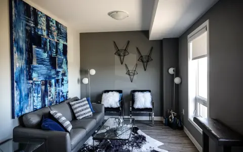 Canapé gris foncé, murs gris anthracite. Une grande toile abstraite bleue et blanche domine le salon moderne.