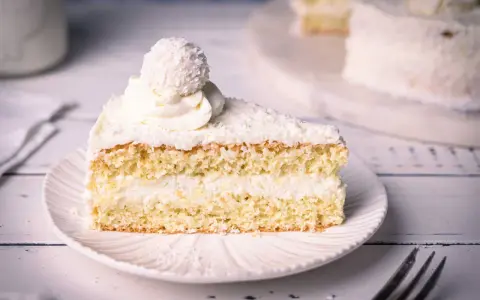Ein saftiges Stück Raffaello Torte mit Kokosraspeln und Sahne, gekrönt von einer Raffaello-Kugel.
