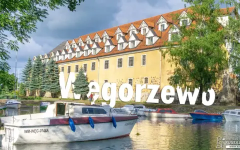 Węgorzewo atrakcje: malowniczy widok na port z łodziami i zabytkową kamienicą. Idealne miejsce na wypoczynek nad jeziorem.