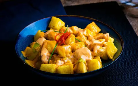 Patatas alioli cremosas y doradas, servidas en un cuenco azul, con un toque de chile rojo y cebollino.