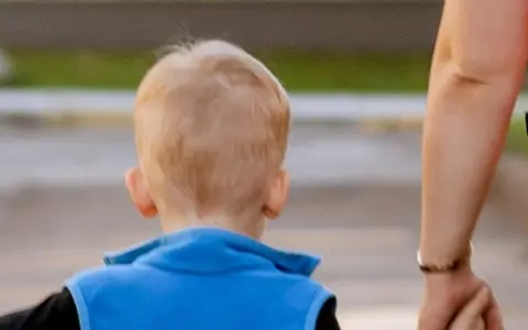 Wskazówki, jak rozmawiać z dzieckiem z aspergerem. Dłoń dorosłego prowadzi dziecko w niebieskiej kamizelce.