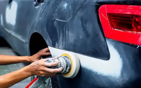 Mechanik szlifuje błotnik samochodu. Pytanie, czy benzyna ekstrakcyjna niszczy lakier, jest ważne przy takich pracach.