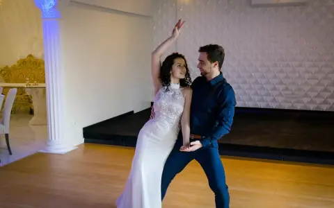 Para tańczy w białej sukni i granatowym garniturze. Ich ruchy są płynne, jakby tworzyli idealny, taneczny duet.