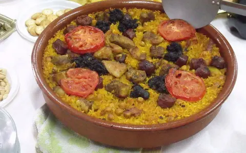 Un delicioso arroz al horno en cazuela de barro, con trozos de carne, chorizo, garbanzos y rodajas de tomate.