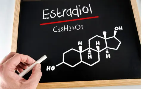 Estradiol co to za badanie? Na tablicy wzór chemiczny estradiolu (C18H24O2) i jego struktura. Ręka z kredą.