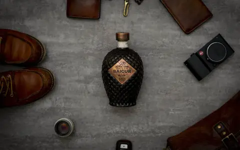 Saigon Baigur Gin mit 43% Alkoholgehalt, umgeben von Lederaccessoires, Kamera und Schuhen.