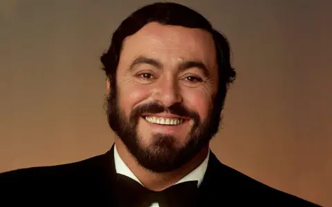 Uśmiechnięty Luciano Pavarotti w czarnym smokingu. Jego głos porusza serca, a jego uśmiech mówi "ti amo".