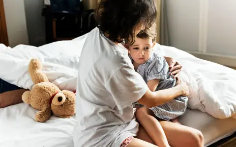 Mutter tröstet ihr Kind, das Anzeichen einer Panikattacke bei Kindern zeigt. Ein Teddybär liegt daneben.