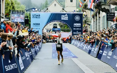 Biegacz z polską flagą przekracza metę UTMB Mont-Blanc. Tłum kibiców świętuje jego sukces.