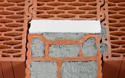 Zbliżenie na pustaki ceramiczne z widocznymi pustymi przestrzeniami i zaprawą. Pokazane są wymiary pustaka i sposób ich układania.