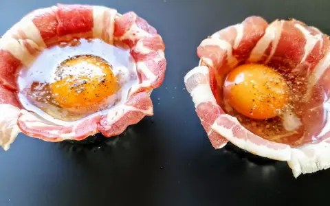 Due uova crude con tuorlo brillante, avvolte in strisce di bacon croccante, pronte per essere cotte.