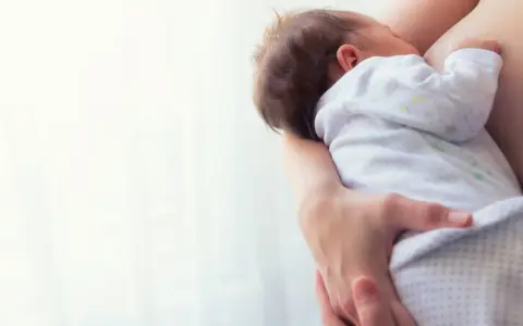Ciepłe objęcia mamy, maluszek karmiony piersią. Delikatne dłonie otulają dziecko, tworząc bezpieczną przestrzeń.