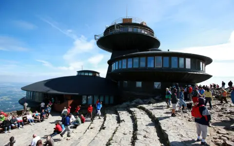 Ludzie odpoczywają na kamienistym szlaku na Śnieżkę, podziwiając widok na budynek obserwatorium.