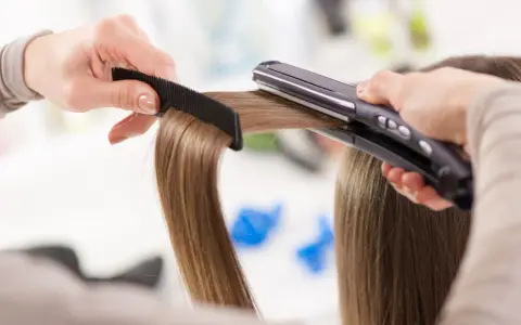 Manos peinando y alisando cabello con una plancha. ¡Sorprendentemente, se puede planchar la ropa con la plancha del pelo!