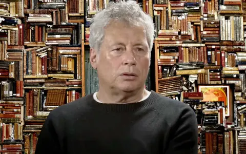 Un uomo con capelli grigi davanti a uno sfondo di libri antichi, forse ispirato ai libri di Alessandro Baricco.