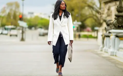 Mujer con estilo **smart casual** camina por la calle con un blazer blanco, jeans oscuros y sandalias de tacón.