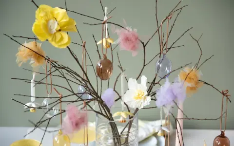 Vacker påskris inspiration med grenar dekorerade med glaskulor, tygblommor och fluffiga dekorationer i pastellfärger.
