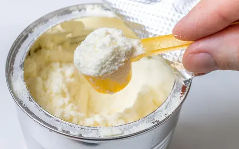 Eine Hand schöpft mit einem gelben Löffel feines Pulver aus einer Dose. Manche denken, dass Proteinpulver dick machen kann, doch es kommt auf die Menge an.