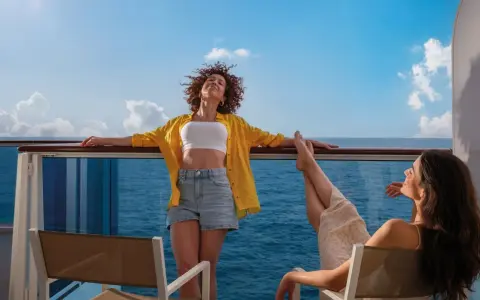 Due donne si godono il sole sul ponte di una nave, con il mare blu all'orizzonte. Una carta costa ideale per una vacanza rilassante.