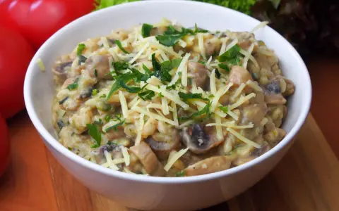 Pyszne risotto z pieczarkami, posypane startym serem i świeżą natką pietruszki, czeka w białej miseczce.