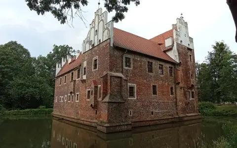 Zamek na wodzie w Wojnowicach, otoczony fosą, prezentuje ceglaną architekturę z białymi zdobieniami.