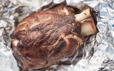 Stinco di maiale succulento, cotto alla perfezione e avvolto in carta stagnola, pronto per essere gustato.