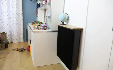 Un radiateur Qarnot particulier noir, surmonté d'un plateau en bois et d'un globe, réchauffe la chambre d'enfant remplie de jouets.
