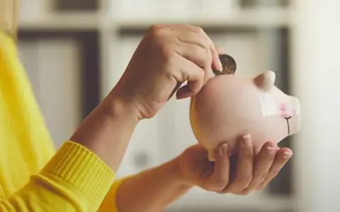 Manos introducen una moneda en una hucha rosa, simbolizando el ahorro para recuperar plan de pensiones nueva ley.